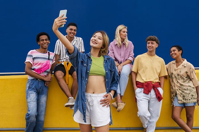 Confident young woman standing in front of group of friends taking a selfie