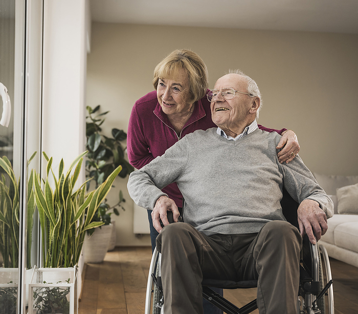 Happy senior woman taking care of man sitting in wheelchair
