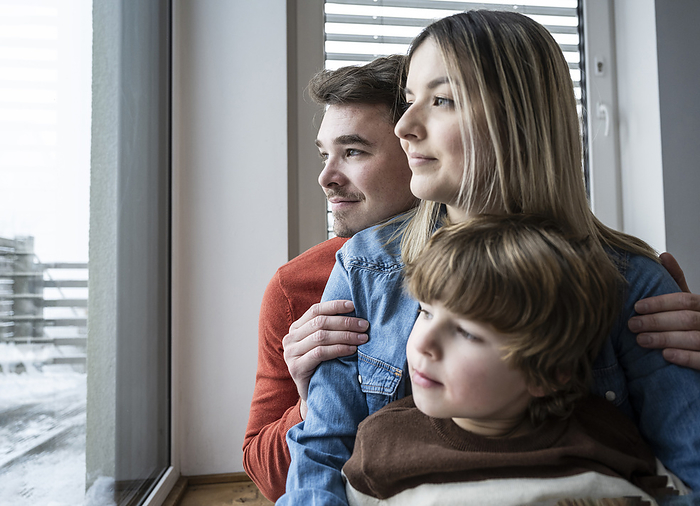 Smiling father and mother with son looking through window at home