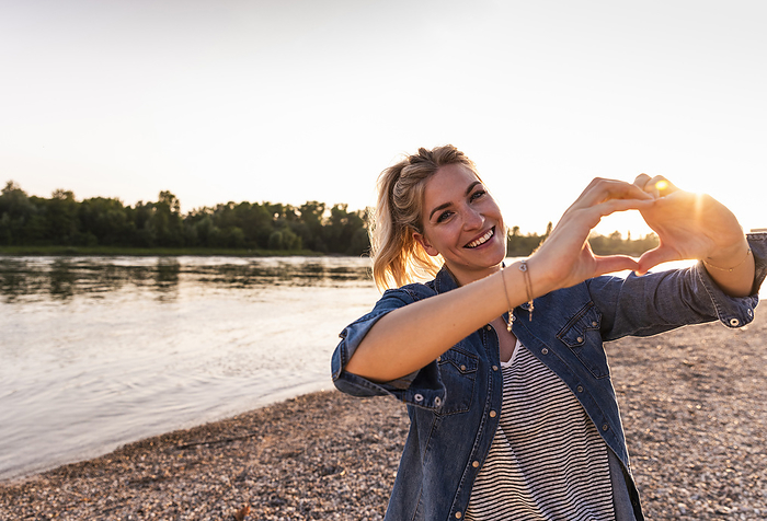 Smiling woman gesturing heart shape at beach