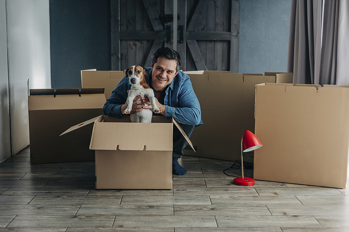 Happy man with dog near cardboard boxes at home