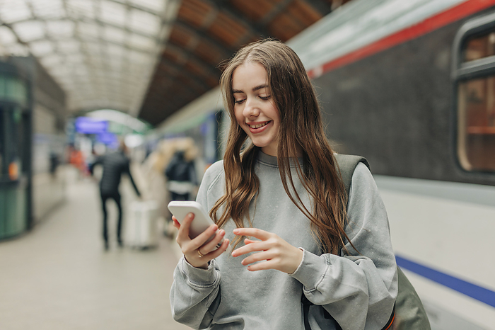 Smiling young woman using smart phone at train station