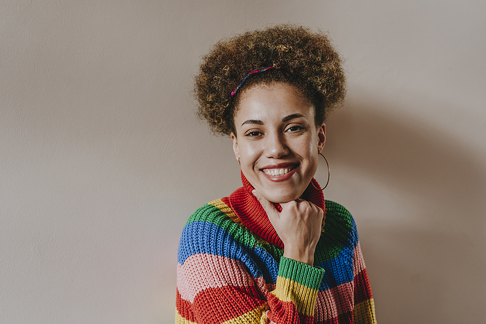 Happy woman wearing multi colored sweater in front of wall
