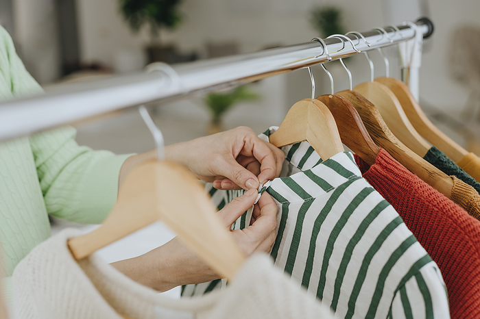Hands of woman choosing clothes from rack at home