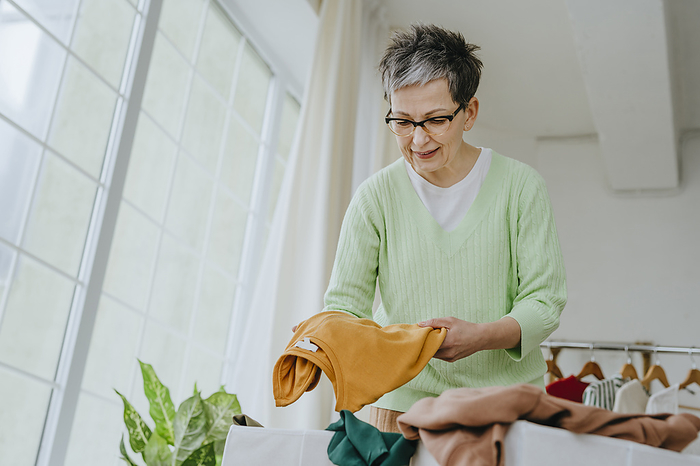 Mature woman folding clothes at home