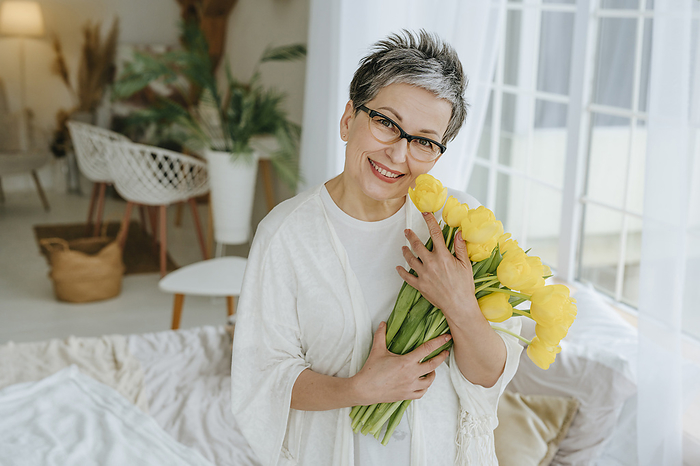 Smiling mature woman holding bunch of tulips at home