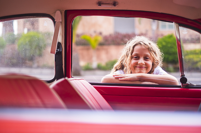 Smiling girl over the car cheerful and happy young girl 8 years old smile and enjoy the day near a red vintage classic car, ready to start and travel before the school, caucasian child in happiness and travel before the school, caucasian child in happiness