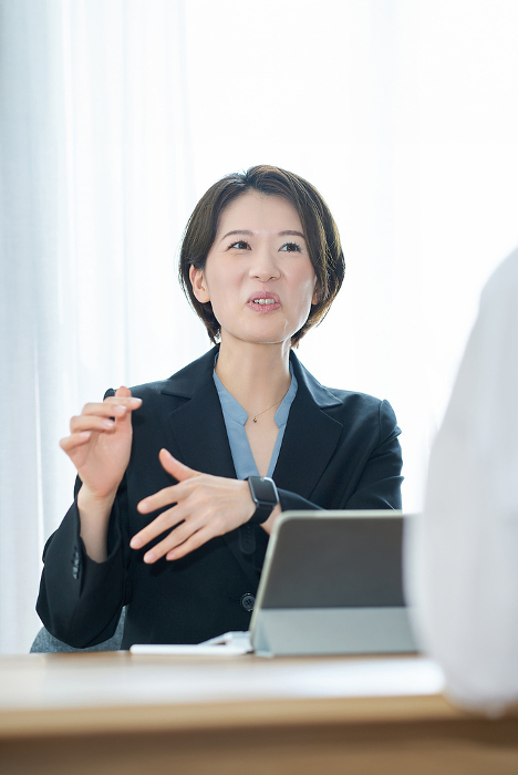 A Japanese woman in a suit explaining to a woman in plain clothes (People)
