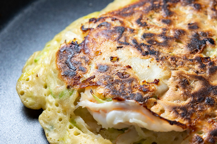 Close-up of cooking scene of okonomiyaki in a frying pan.
