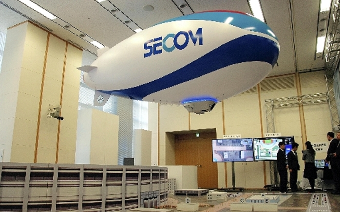 SECOM s public mock up exercise of a security airship   Security service by SECOM and airship from the sky A mock up exercise of a security airship unveiled by SECOM. In the back is a surveillance monitor. Photographed in Shibuya Ward, Tokyo, on December 24, 2014. SECOM s airship based crime prevention service appeared in the morning edition of the same month on December 25.  On December 24, SECOM, the largest security company in Japan, unveiled its first security monitoring service using an airship. The service, which can be monitored from the sky with cameras, will be useful for security of dignitaries and analysis of congestion at large events. The airship is unmanned, 15 meters long and 4 meters wide, and can reach a maximum speed of 50 km h. On the 24th, a demonstration was held using a prototype one third the size of the actual airship.