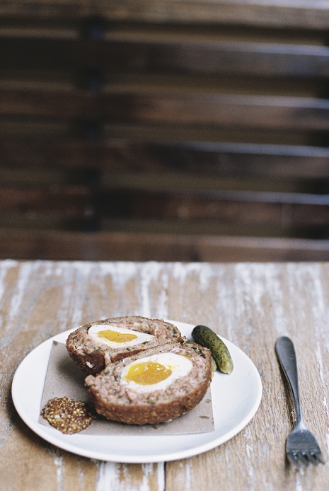 A meal on a plate, a scotch egg cut in half with garnishes.