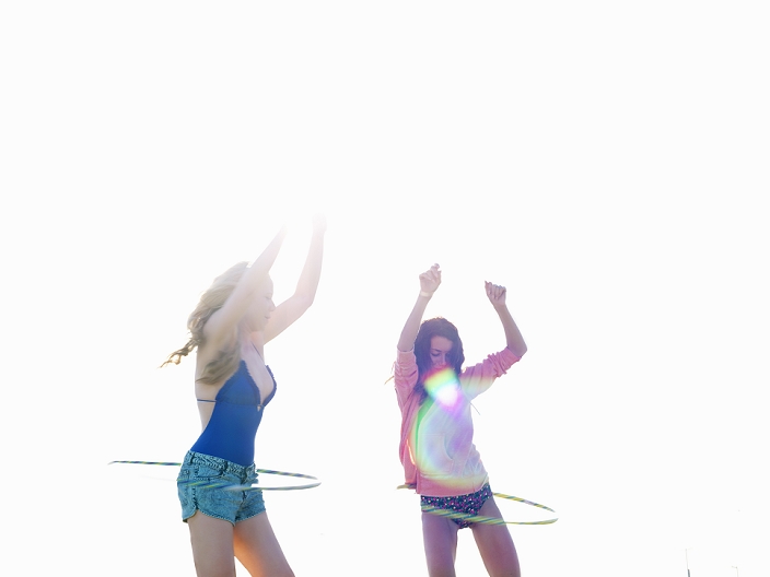 Two young women friends swinging hoola hoops on beach, Williamstown, Melbourne, Australia