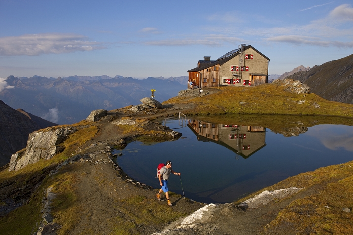 A male hiker at the lake of the beautiful located Sudetendeutsche mountain hut during the Glocknerrunde, a 7 stage trekking from Kaprun to Kals around the Grossglockner, the highest mountain of Austria.     Located in the heart of the Hohe Tauern National Park which contrasts impressive, glacier-covered high alpine scenery with an alpine farming landscape carefully cultivated for centuries, the Glockner Circuit offers a unique nature and walking experience.    At the end of each day?s walk, mountain shelters or alpine inns beckon to rest, eat and get a good night?s sleep. Alpine huts are equipped and operated only with the basic essentials because of the difficulties in bringing in supplies and disposing of waste, the altitude, the extreme climate and the often long ascents! After any stage of the walk, you have the opportunity to leave the Glockner Circuit and walk down to the National Park villages of Kaprun, Uttendorf, Kals, Heiligenblut or Fusch to spend the night in a guesthouse, inn or hotel.    The tour mainly spans high alpine terrain but can be negotiated by anyone with some alpine experience and corresponding fitness and equipment, as there are no glaciers or roping sections along the circuit. A head for heights and surefootedness are necessary.   Photo by Menno Boermans / Aurora Photos