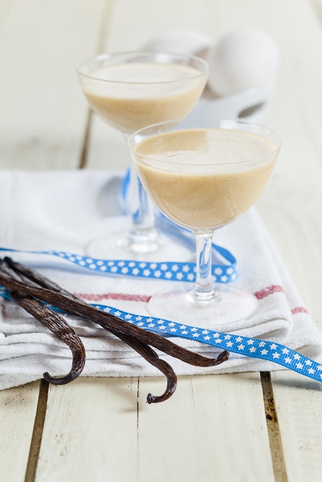 Two glasses of egg liqueur, ribbon and vanilla beans on cloth