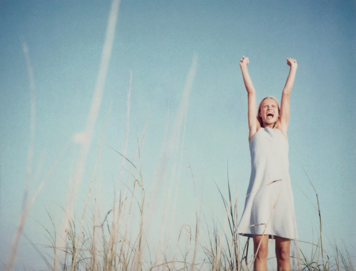 female Young woman standing in field with arms raised, shouting, low angle view