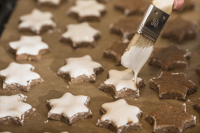 Close-up of a woman icing star shape cinnamon with basting brush, Munich, Bavaria, Germany