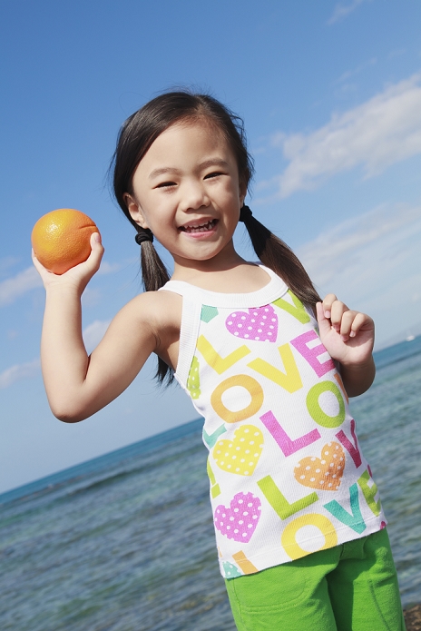 A young girl holds an orange and poses for the camera at the water's edge;Honolulu oahu hawaii united states of america