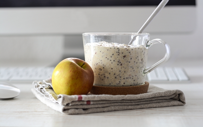 Glass of porridge with linseed and chia seed and an apple on desk