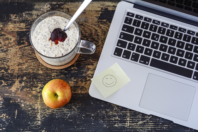 Glass of porridge with jam, linseed and chia seed, apple and laptop on wood
