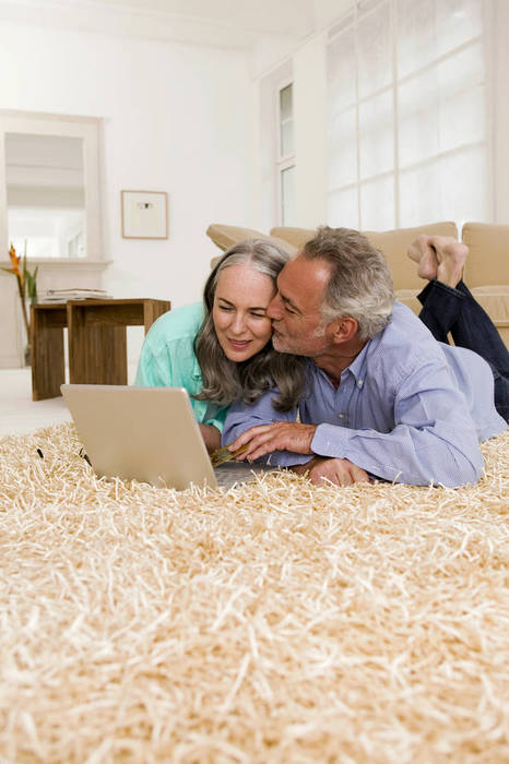 WESTF01883 Mature couple lying on carpet with laptop, man kissing woman