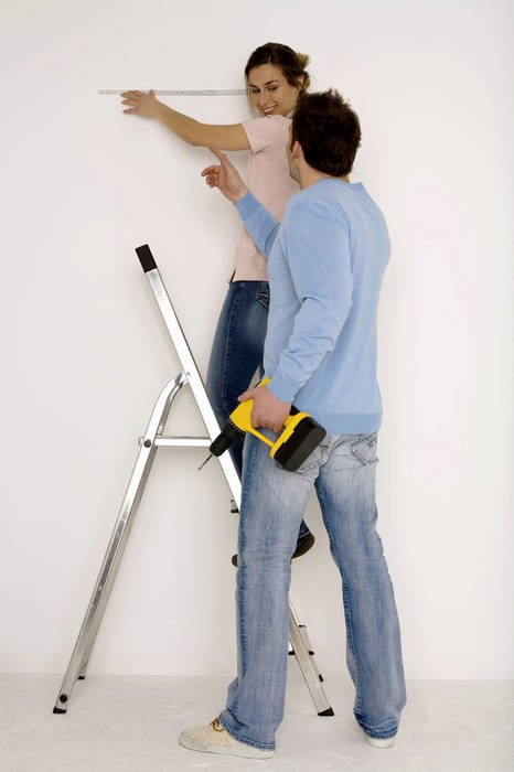 WESTF00574 Young couple, man holding electric drill, woman measuring wall with scale