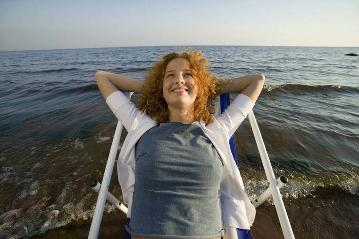 WESTF01775 Young woman relaxing in deck chair on beach, smiling, close up