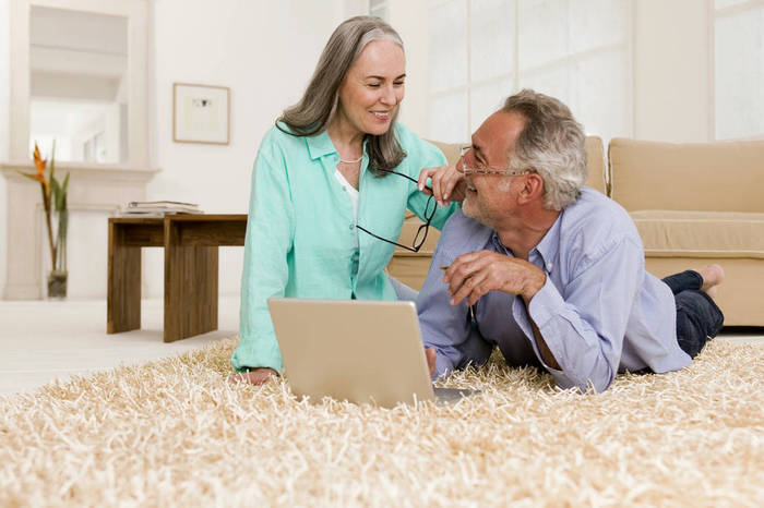 WESTF01879 Mature couple lying on carpet with laptop, smiling