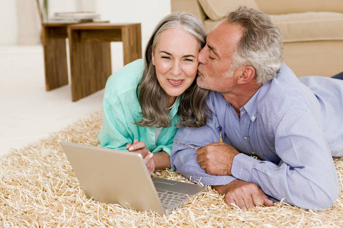 WESTF01882 Mature couple lying on carpet with laptop, man kissing woman