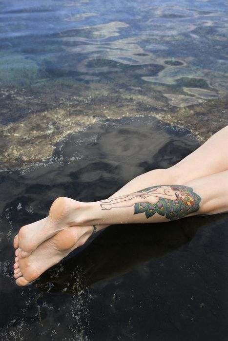 Legs of tattooed Caucasian woman lying in tidal pool in Maui, Hawaii, USA.