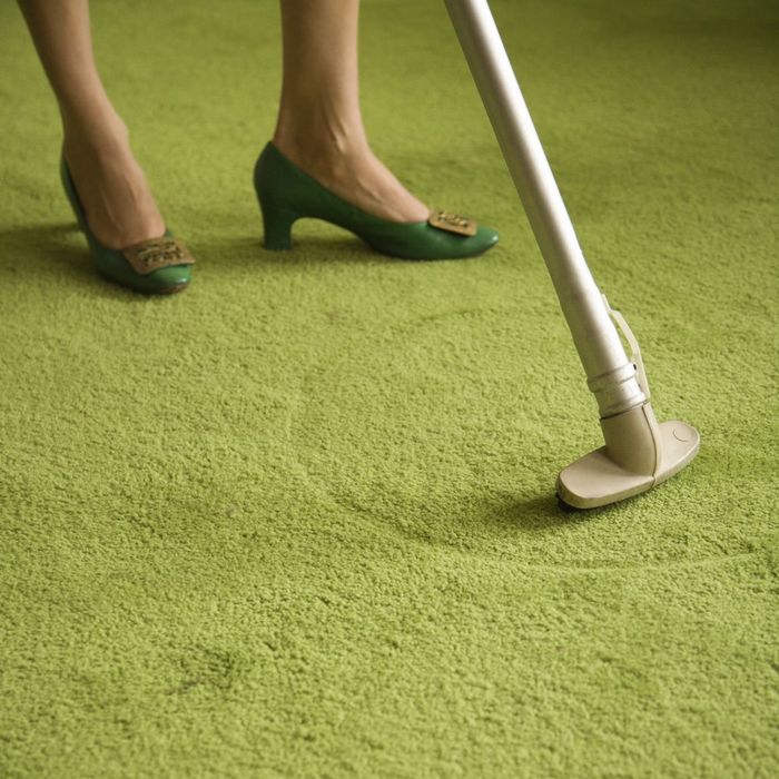 Close-up of Caucasian female feet with vacuum extension against green retro carpet.