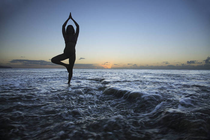Woman doing yoga Hawaii, Oahu, Fit young girl on the beach doing yoga on the rocky coastline.