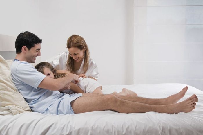 Mid adult couple smiling with their daughter on the bed