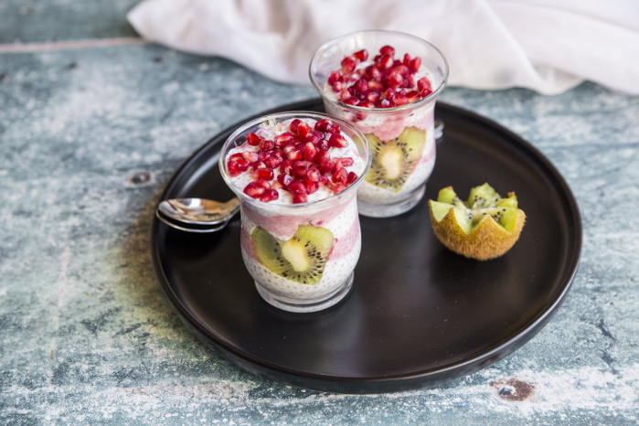 Two glasses of chia pudding with heart-shaped kiwi slices and pomegranate seed on tray