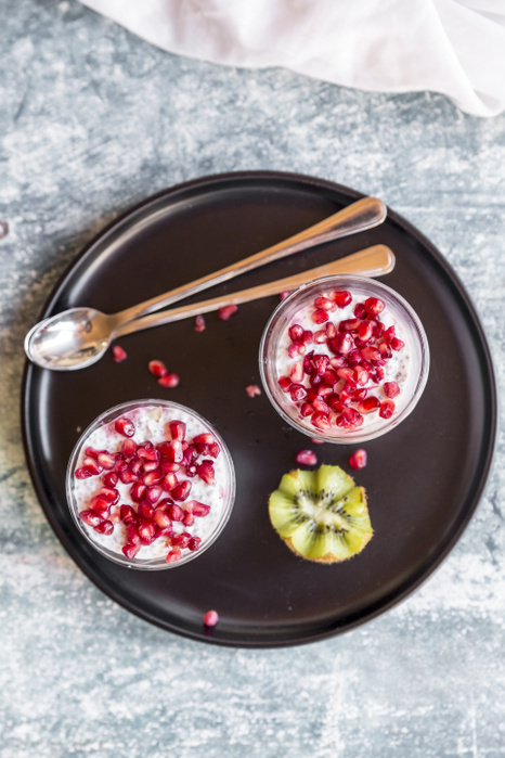 Two glasses of chia pudding with kiwi  and pomegranate seed on tray