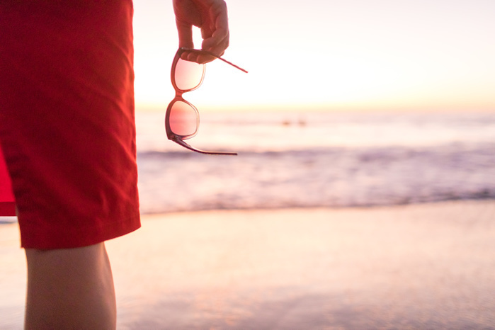   Rear cropped view of woman s hand holding sunglasses on beach at sunset, Nosara, Guanacaste Province, Costa Rica