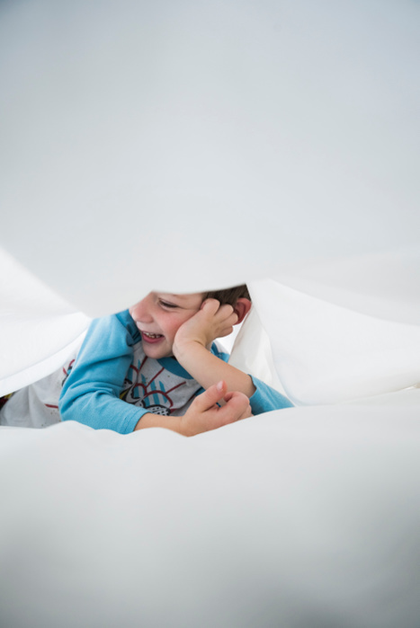   Boy lying on side between white bed sheets