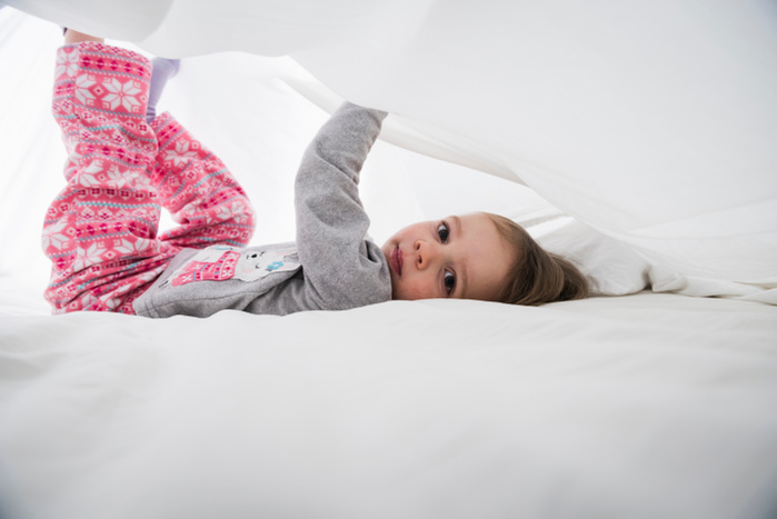   Portrait of female toddler lying between white bed sheets