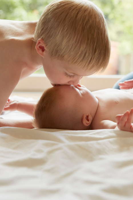   Boy leaning forward to kiss baby brother on forehead