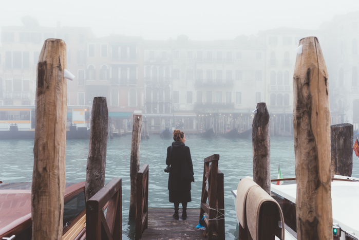   Rear view of woman looking out from misty canal pier, Venice, Italy