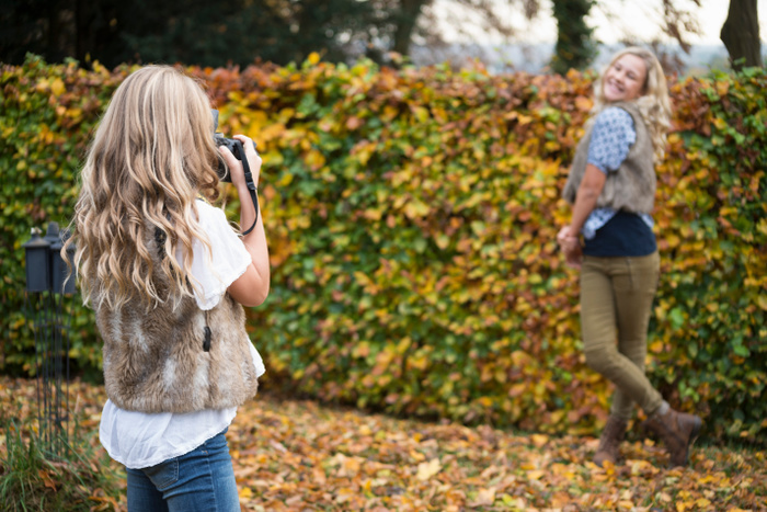 Girl photographing sister by autumn garden hedge
