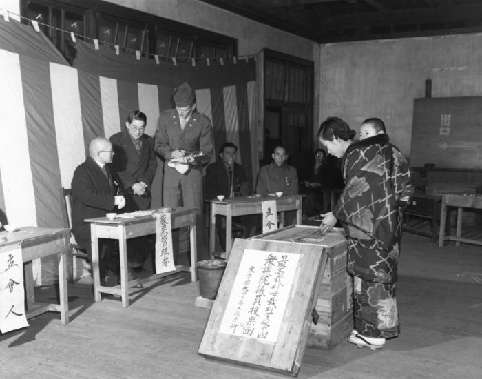 1949 Election to the House of Representatives A woman carrying a child on her back in the traditional way also casts a vote in a sealed ballot box. Sergeant Huff oversees the voting with the help of an interpreter. A voting booth in Ota Ward, Tokyo, on 1 23 1949  Photo by Kingendai Photo Library AFLO  2373 .