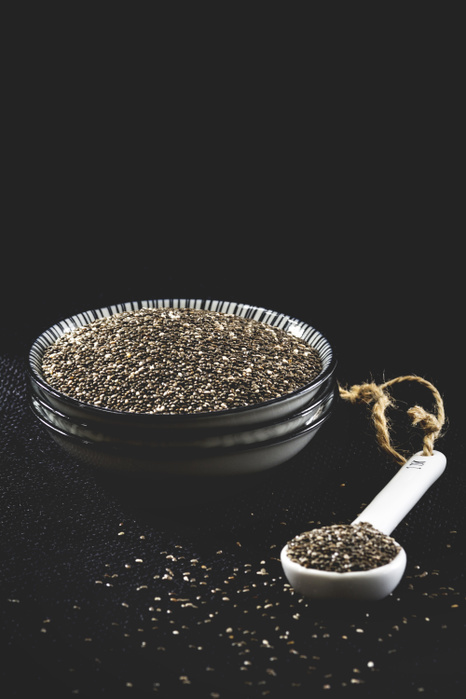 Bowl and mass of black chia seeds on black ground