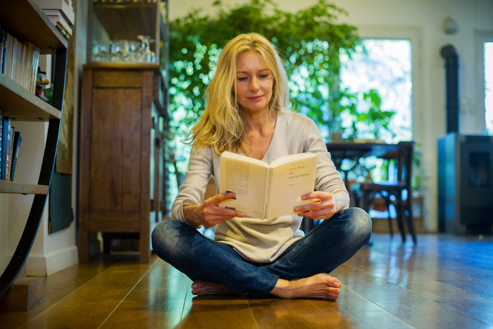 Woman reading Mature woman sitting on floor at home, reading book