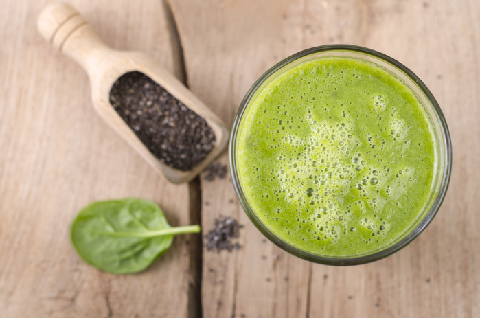 Glass of spinach smoothie, shovel of chia seeds and spinach leaf on wood