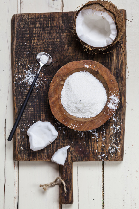 Opened coconut and wooden bowl of coconut flakes on wooden board