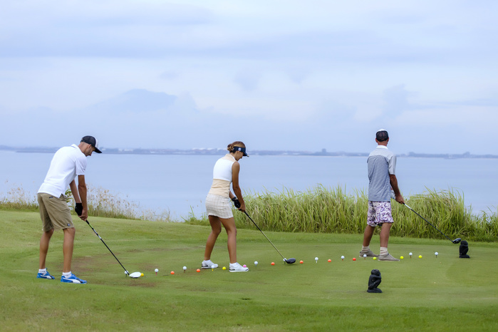 Three people practice driving golf balls with ocean in background Golf players and ocean in background,Bali,Indonesia
