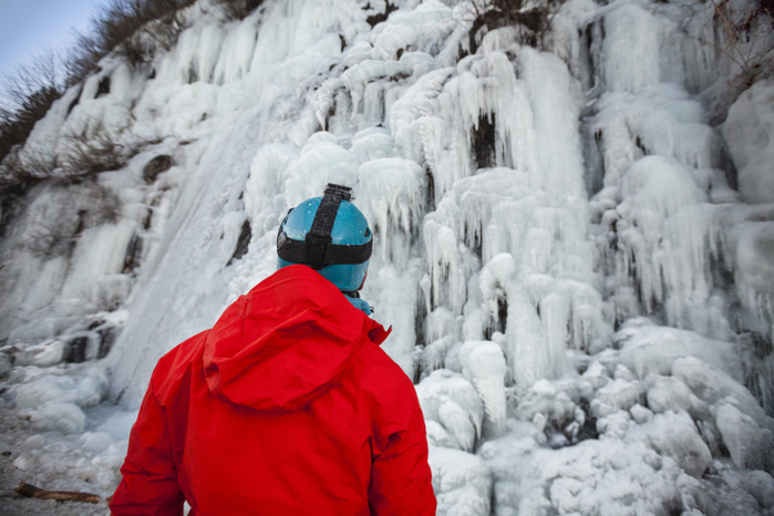 Rear view of climber in red jacket looking at hill in ice Ice climbing at the Trojan Horse, a roadside ice flow near Harrison Hot Springs, British Columbia, Canada.