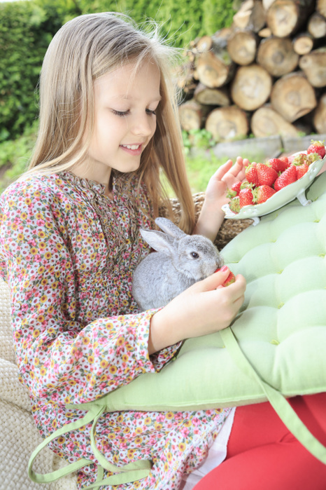 Smiling girl feeding rabbit with strawberries