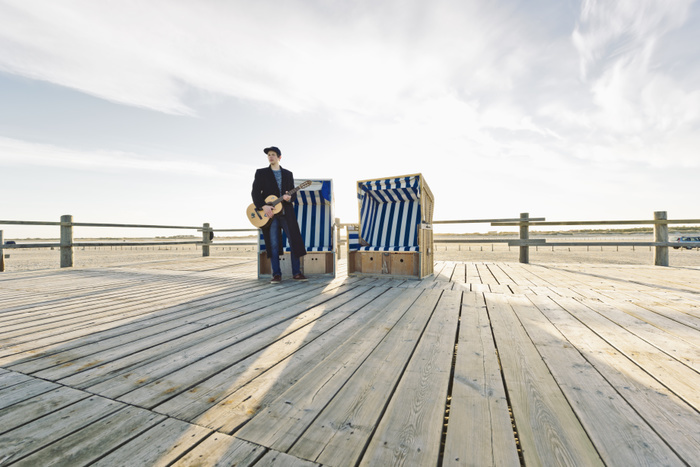 Germany, Sankt Peter-Ording, teenage boy with guitar standing in front of hooded beach chair