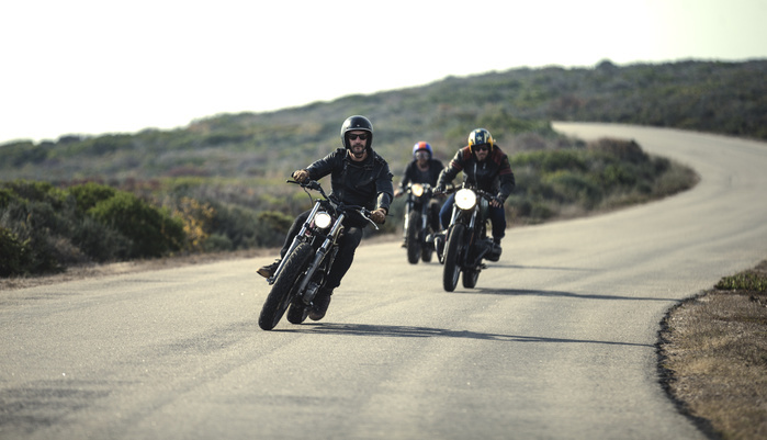 Three men wearing open face crash helmets and sunglasses riding cafe racer motorcycles along rural road. Three men wearing open face crash helmets and sunglasses riding cafe racer motorcycles along rural road.